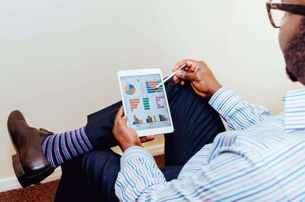 Man in striped dress shirt and striped socks views data and analytics on a tablet to inform business decisions.
