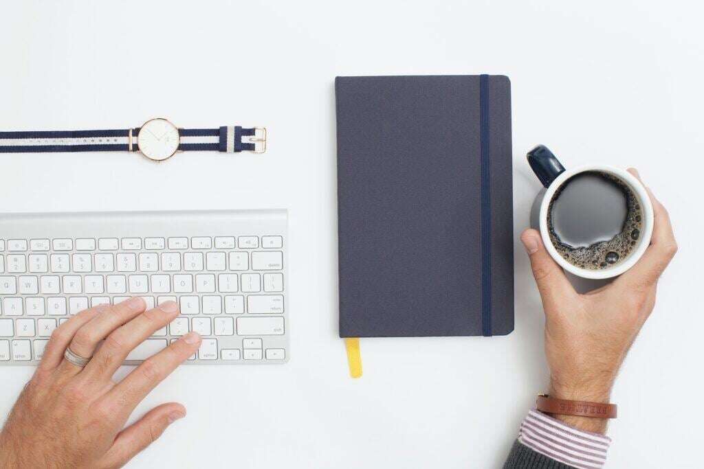 Image of a desk with keyboard, watch, planner and coffee