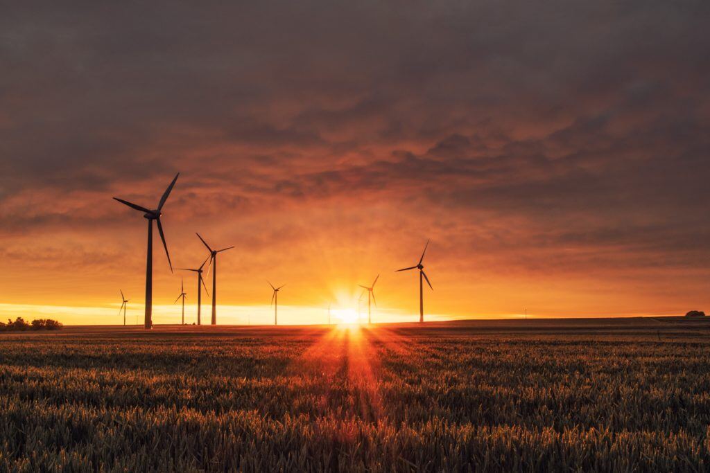 Image shows wind turbines against a sunset backdrop.
