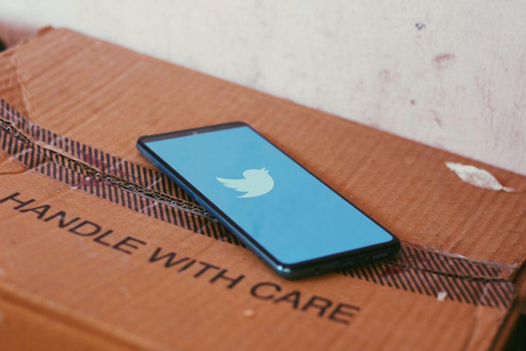 A cell phone logged into Twitter rests on a box labeled "handle with care."